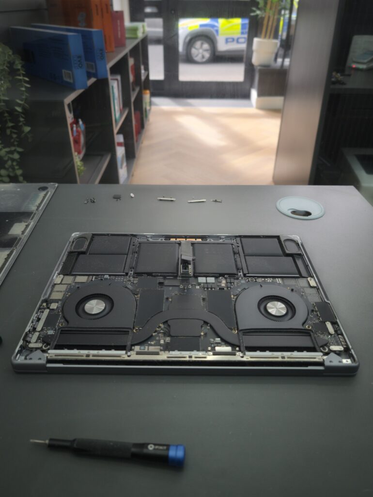 MacBook Pro 16 back cover removed revealing the logic board, twin cooling fans, battery cells and the row of screws lined up for reassembly