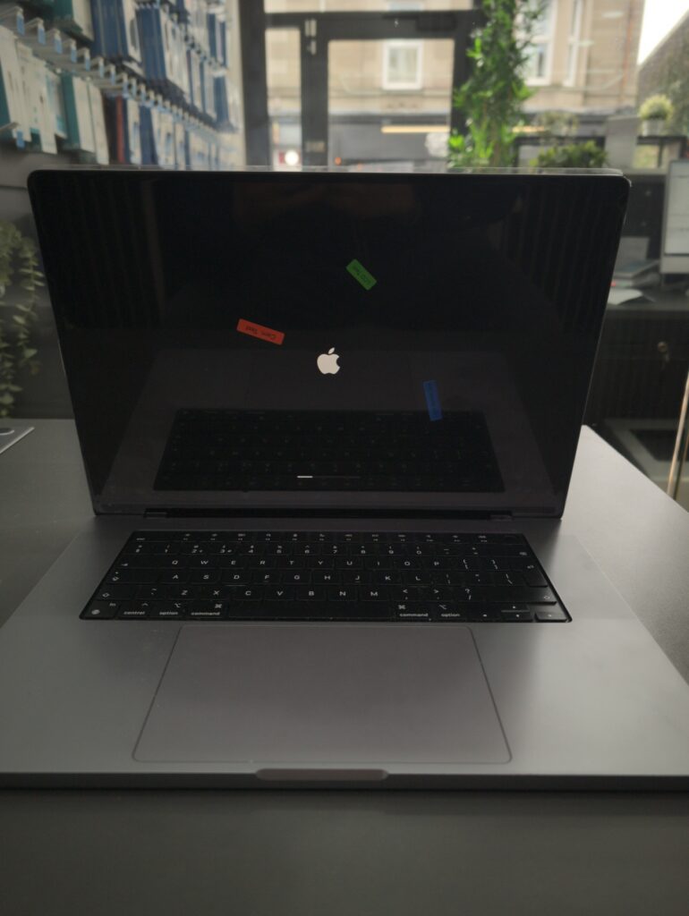 MacBook Pro 16 rebuilt and powered on, with the factory QC stickers still on the protective film of the new replacement display assembly