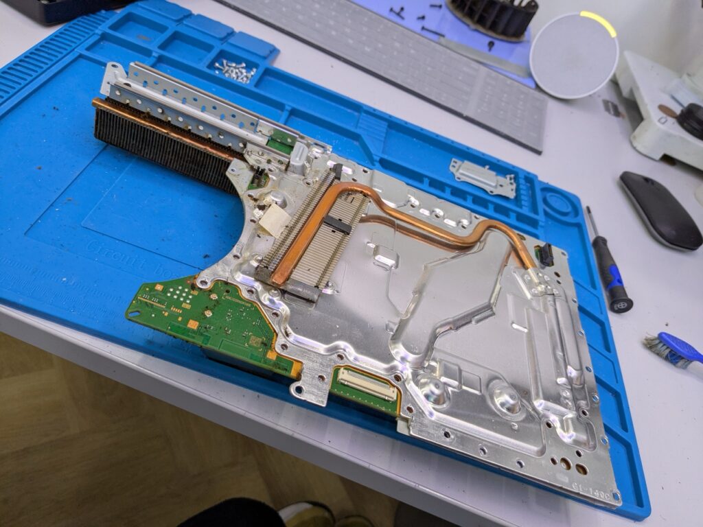 PlayStation 5 Slim cooling shroud and copper heat pipes lifted out of the chassis, sitting on the bench