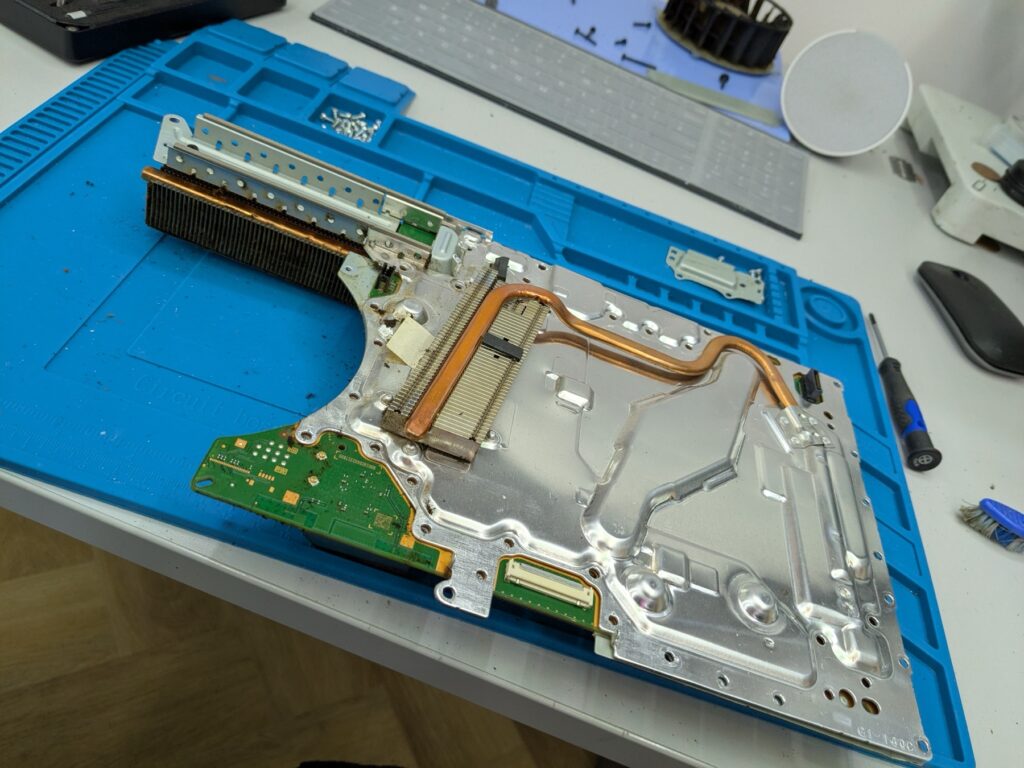 Underside of the PlayStation 5 Slim logic board still attached to the silver heatsink stack with copper heat pipes routing across the surface