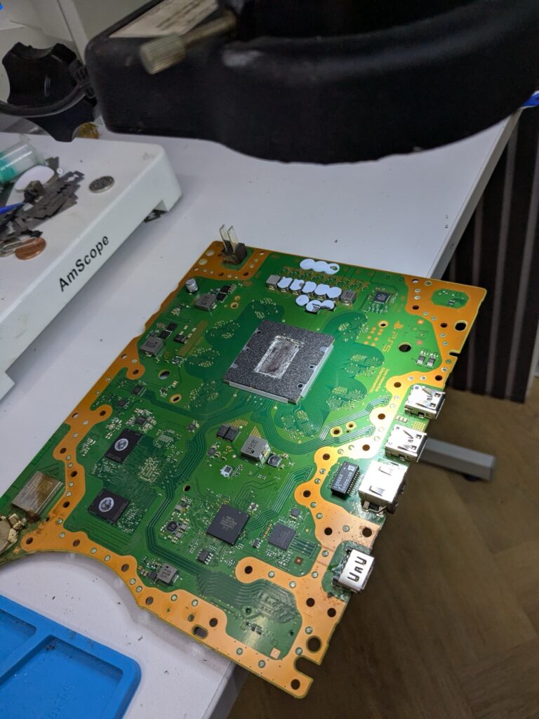 Top side of the PlayStation 5 Slim logic board showing the central SoC under its silver heat-spreader shield and the surrounding power circuitry